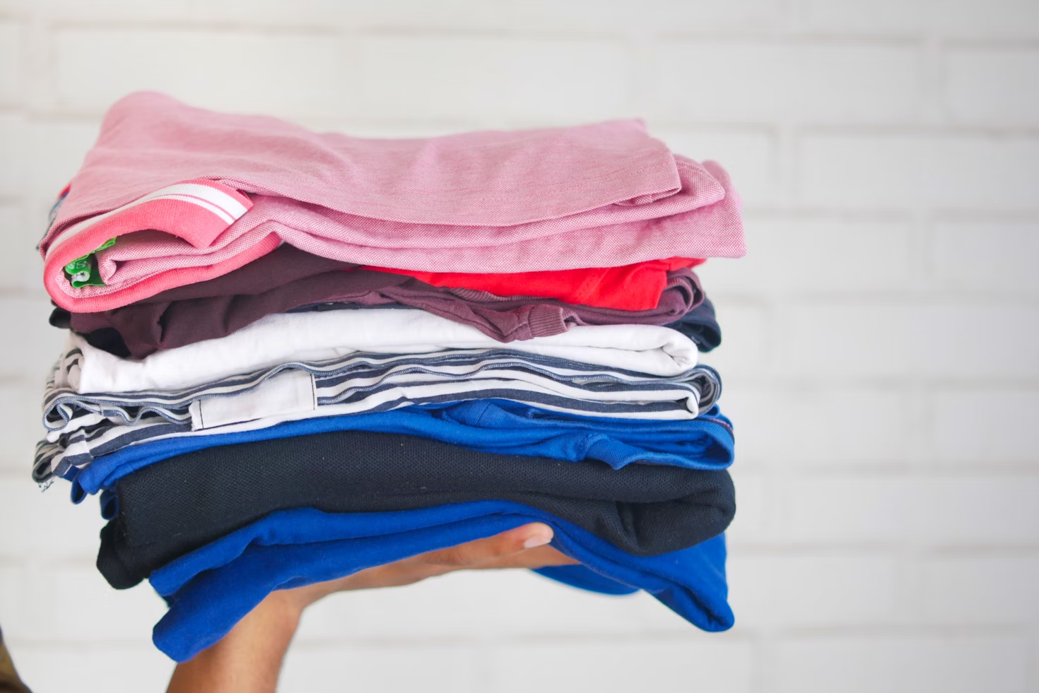The image shows a stack of neatly folded clothes held in a person's hand.