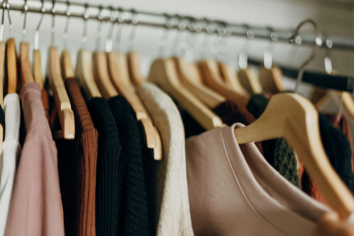 The image shows a close-up of various sweaters hanging on wooden hangers in a closet.