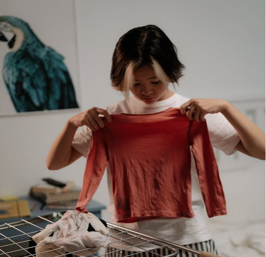 The image shows a person hanging clothes on a drying rack and holding a red shirt.