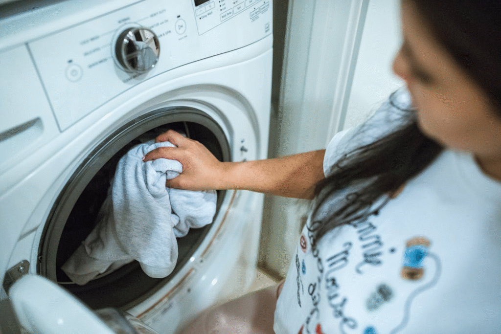The image shows a person putting clothes into a washing machine.