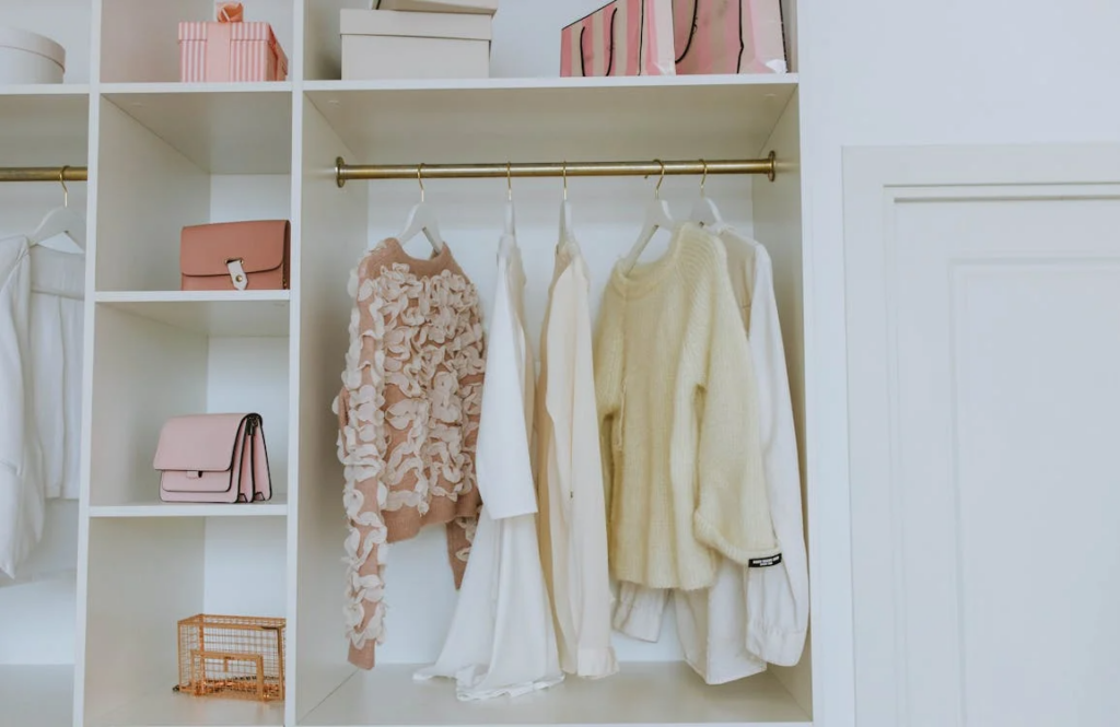 A neatly organized white wardrobe displays pastel clothing and accessories hanging and arranged on shelves.