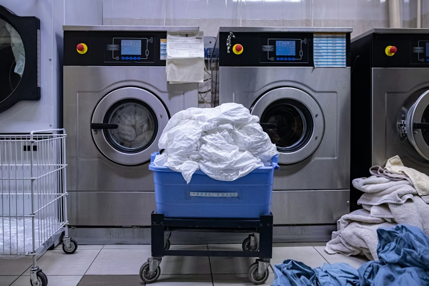 This photo shows a laundry cart in front of some washing machines.