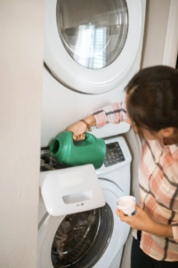 This photo shows an adult pouring laundry detergent into a home washing machine.