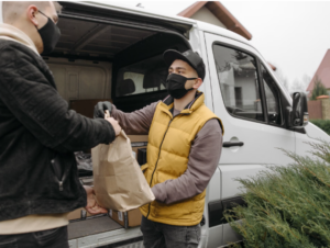This image shows laundry pickup professional handing a customer's bag beside a delivery van.