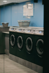 This image shows a row of front-loading commercial washing machines with laundry baskets on top in a clean laundry facility.